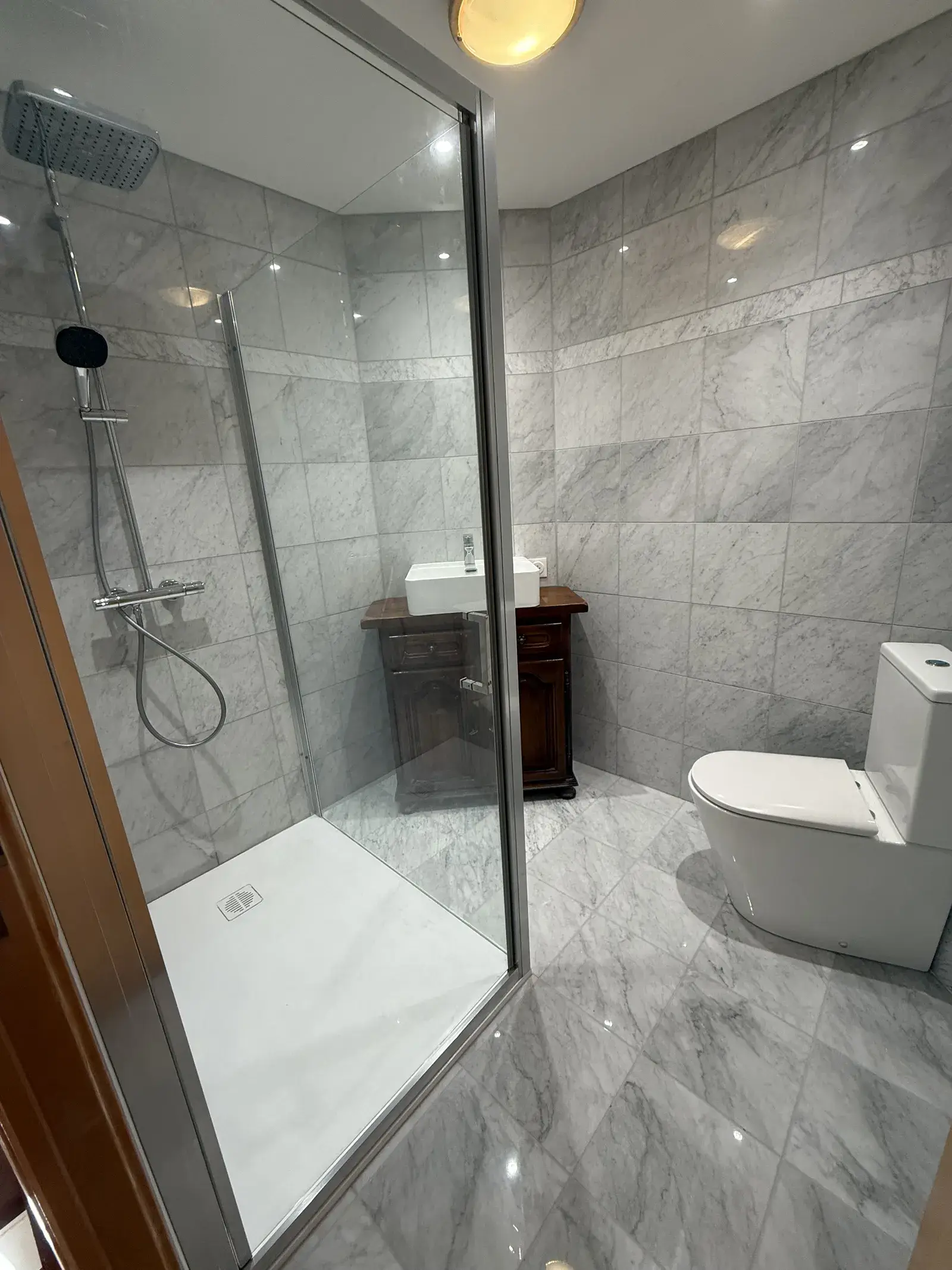 Salle de bain rénovée avec douche, WC et revêtement effet marbre
